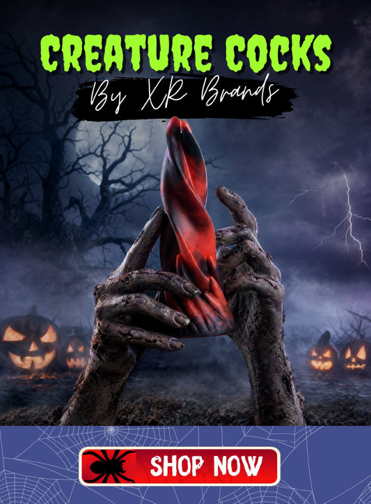 A Halloween-themed promotional graphic with the text 'CREATURE COCKS By XK Brands' at the top and a 'SHOP NOW' banner at the bottom. A pair of skeletal hands holds a glossy red and black novelty item against a dark spooky background with bare trees, lightning, and jack-o'-lanterns.