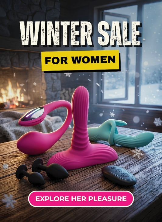 Promotional winter sale graphic for women's intimate products, showing a pink curved wand massager, a teal silicone sleeve, and black bullet-style pieces on a wooden table in front of a fireplace and window. Large text reads 'WINTER SALE FOR WOMEN' and 'EXPLORE HER PLEASURE'.